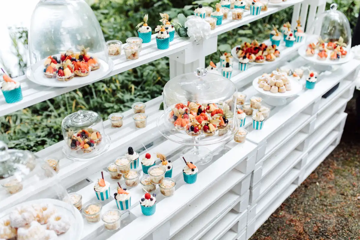 Detailansicht eines Candy Buffets im Freien mit Cupcakes, Desserts im Glas und fruchtigen Mini-Törtchen, dekoriert für Sommerhochzeit.