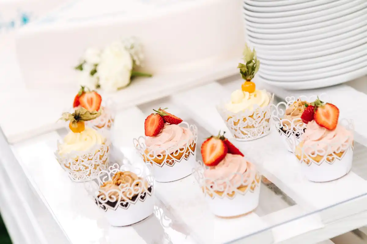 Cupcakes mit rosa und weißer Creme, dekoriert mit Erdbeeren und Physalis, in weißen Spitzenmanschetten.