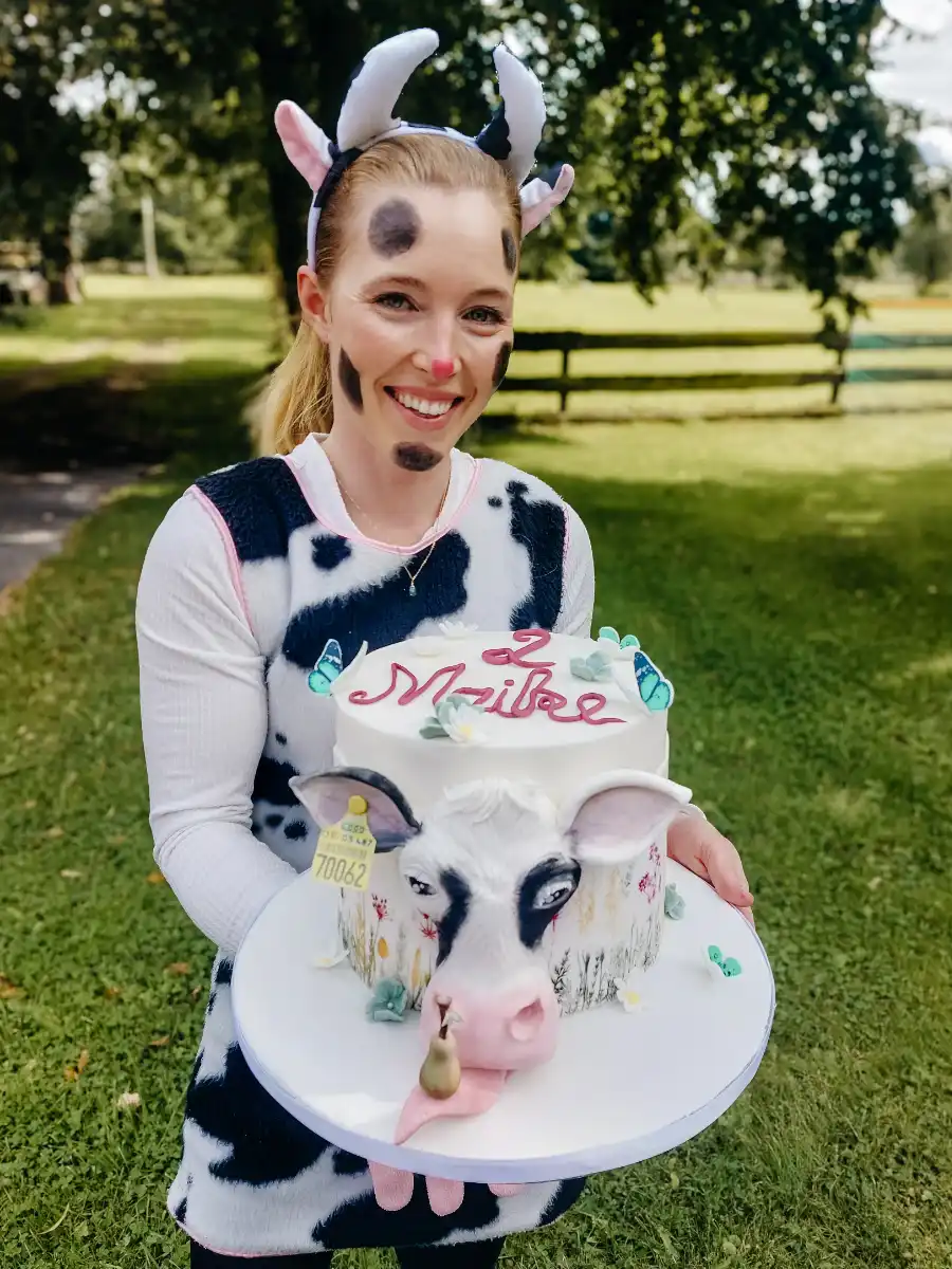 Konditormeisterin Luise Strothenke präsentiert eine Geburtstagstorte als Kuh-Kopf und trägt dazu ein Kuh-Outfit.