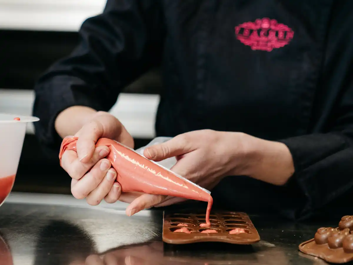 Handgemachte Pralinen in der Herstellung Handwerkliche Herstellung von Pralinen – Konditorin füllt rosa Schokolade in eine Form