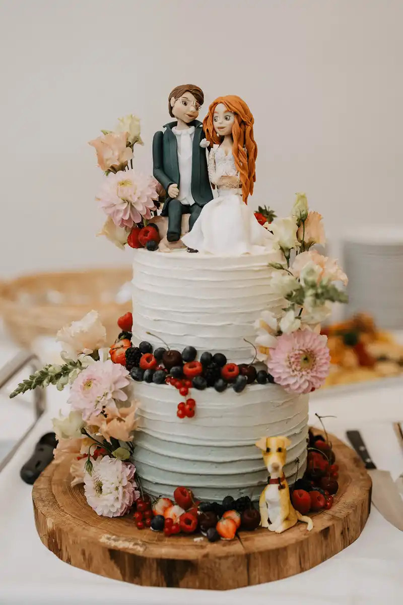 Hochzeitstorte mit Brautpaar-Figuren, Hund, frischen Beeren und Blüten, rustikal präsentiert auf Holzuntersetzer, Dallmanns-Deele Herford